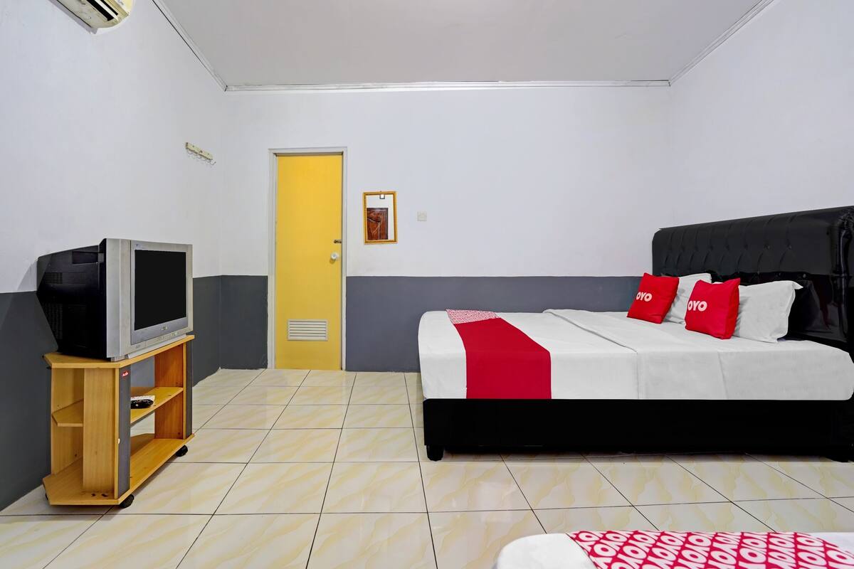 Une chambre d’hôtel avec un lit, un téléviseur posé sur un meuble en bois, une porte et un petit tableau accroché au mur.
