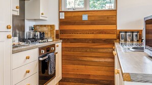 A compact kitchen with wooden paneling, a stove, oven, and a window with a view of greenery.