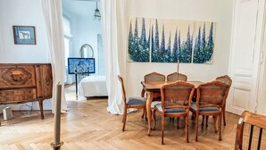 A dining area with a wooden table and chairs, a chandelier, and a painting of trees on the wall.