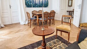 A dining area with a round table, six wooden chairs, and a painting of trees on the wall.