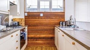 A compact kitchen with wooden paneling, a window with a view, and basic amenities. - Gwithian Premier Lodge (Mullion Cove, Helston)