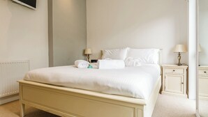 A neatly made bed with pillows and a rolled towel, a bedside table with a lamp, and a wall-mounted TV. - Gwithian Premier Lodge (Mullion Cove, Helston)