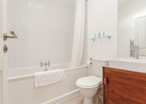 A bathroom with a bathtub, toilet, and a wooden vanity.