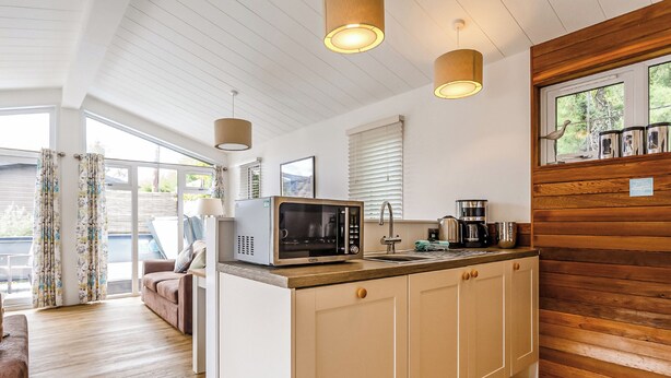 A compact kitchen with a microwave, coffee maker, and wooden cabinets. - Harbour Premier Lodge (Mullion Cove, Helston)