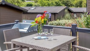 A patio with wicker furniture, a table, a vase with flowers, and a grill. - Harbour Premier Lodge (Mullion Cove, Helston)