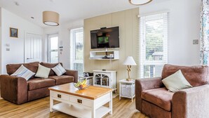 A living room with two brown sofas, a wooden coffee table, a TV, and a lamp. - Harbour Premier Lodge (Mullion Cove, Helston)