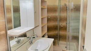 Un baño con lavamanos blanco, espejo y cabina de ducha.