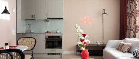 Una cocina moderna con gabinetes blancos, un comedor con mesa y sillas, y una sala de estar con sofá y un florero.