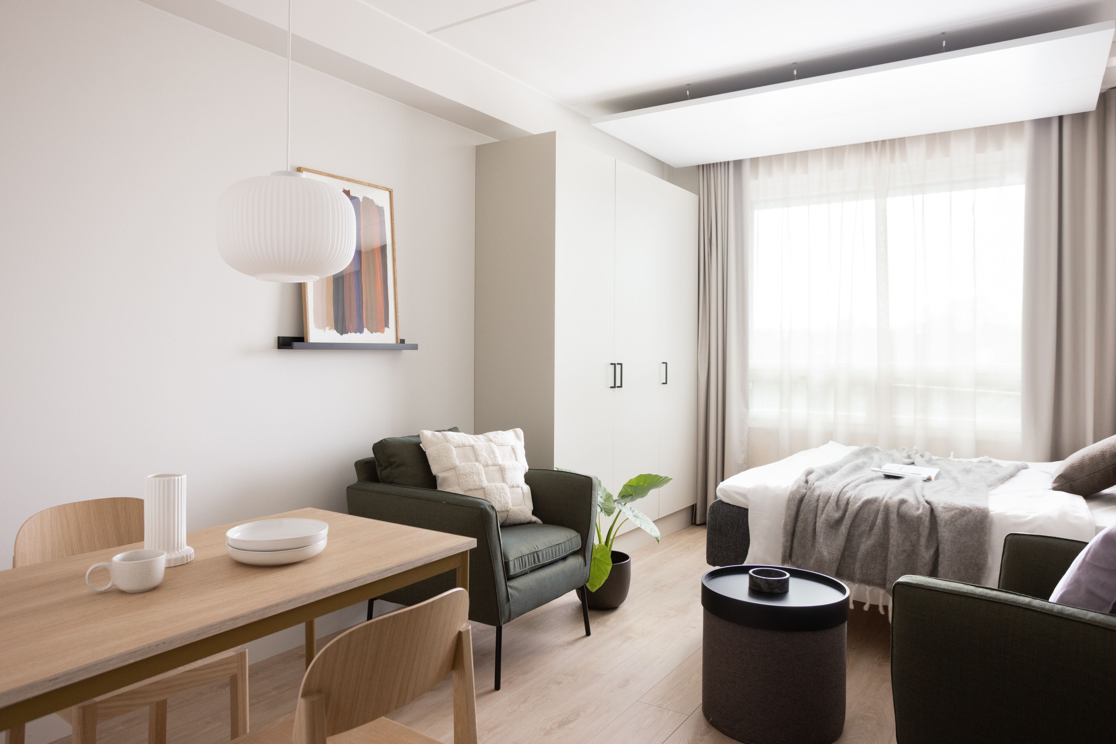 Une chambre d’hôtel moderne avec une table à manger en bois, un canapé, un lit et une grande fenêtre avec des rideaux.