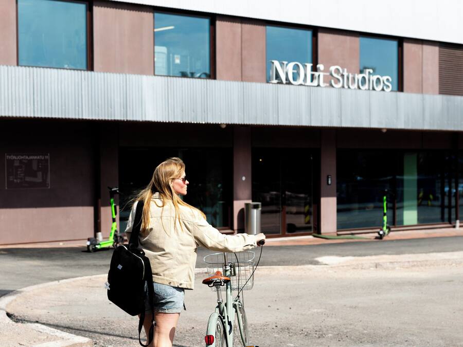 Una persona con una bicicleta frente a un edificio con un letrero que dice "NOLi Studios".