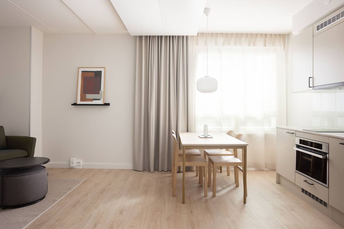 A modern kitchen with a dining area, featuring a wooden table and chairs, a hanging pendant light, and a built-in oven.