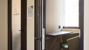 A phone booth with a sign, a small table, and a single chair in a room with a window.