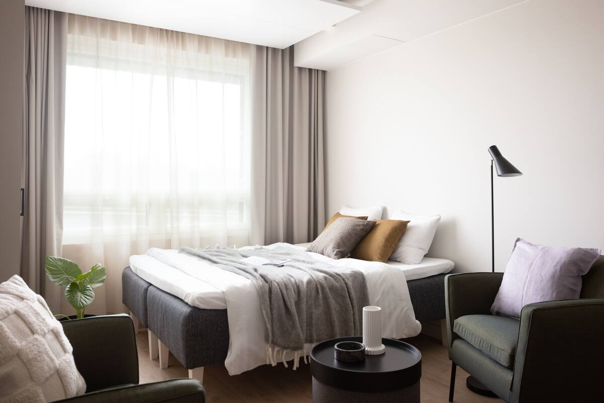 A modern bedroom with a bed, a chair, a bedside table, and a floor lamp.
