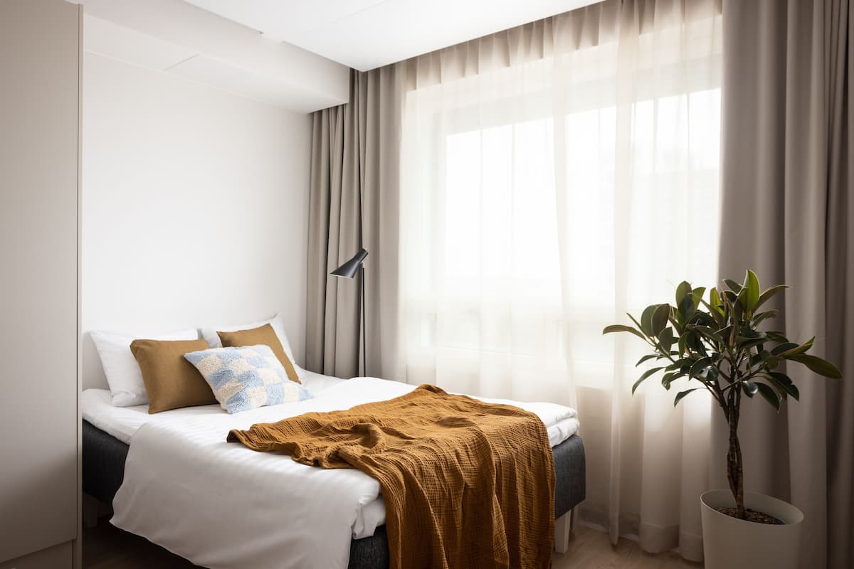 A modern bedroom with a bed, a potted plant, and sheer curtains.