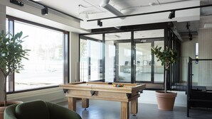 Un espacio interior moderno con mesa de billar, asientos cómodos, ventanas amplias y plantas en macetas.