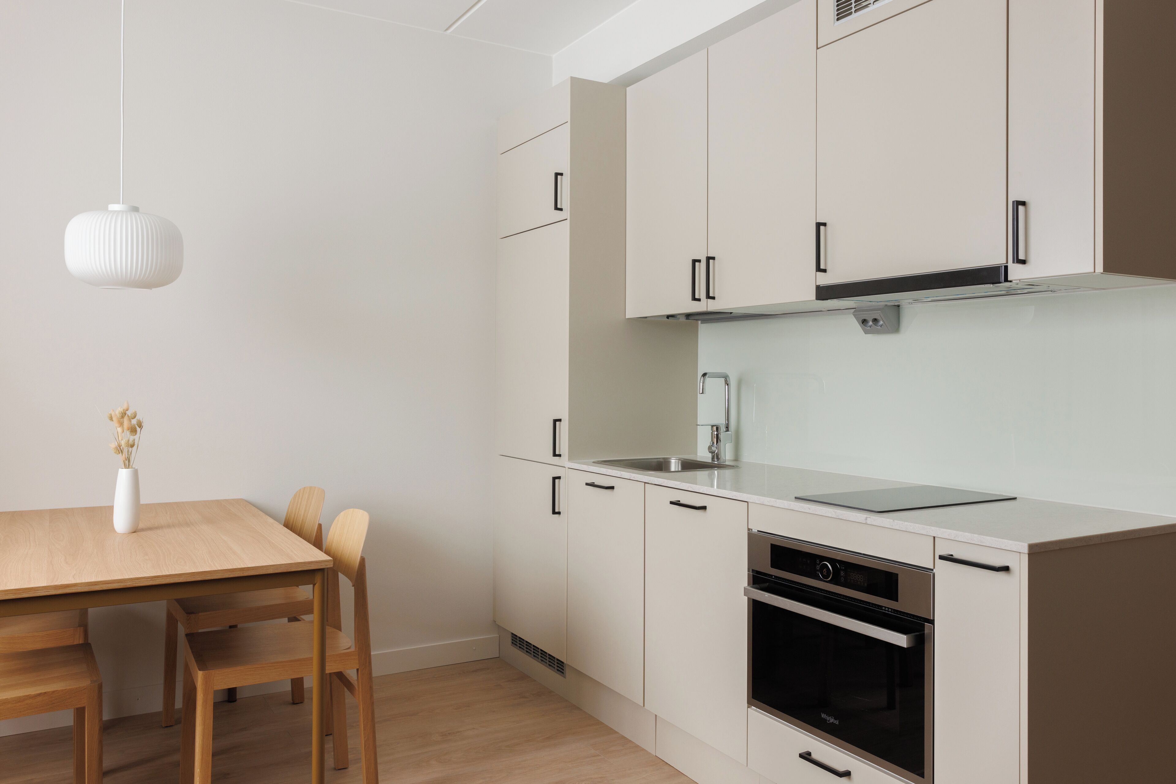 Una cocina moderna con armarios blancos, una mesa de comedor de madera y una lámpara colgante.
