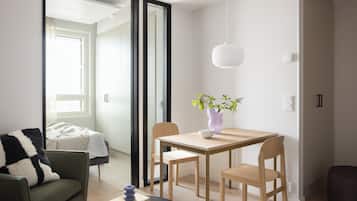 Una sala de estar moderna con un sofá, una mesa de comedor con sillas, una mesita auxiliar con un libro y un objeto decorativo, y una planta en maceta sobre la mesa.