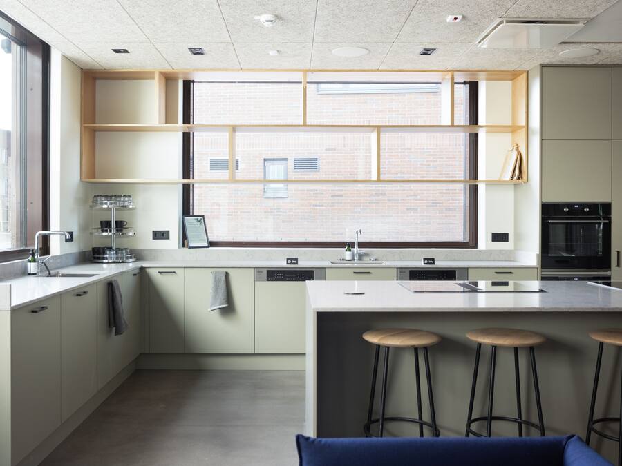 Een moderne keuken met een groot raam, inbouwkasten, een centraal eiland met krukken, en een vaatwasser.