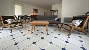 Ein modernes Wohnzimmer mit einem grauen Sofa, Holzstühlen, einem Holztisch und einem sechseckig gefliesten Boden.