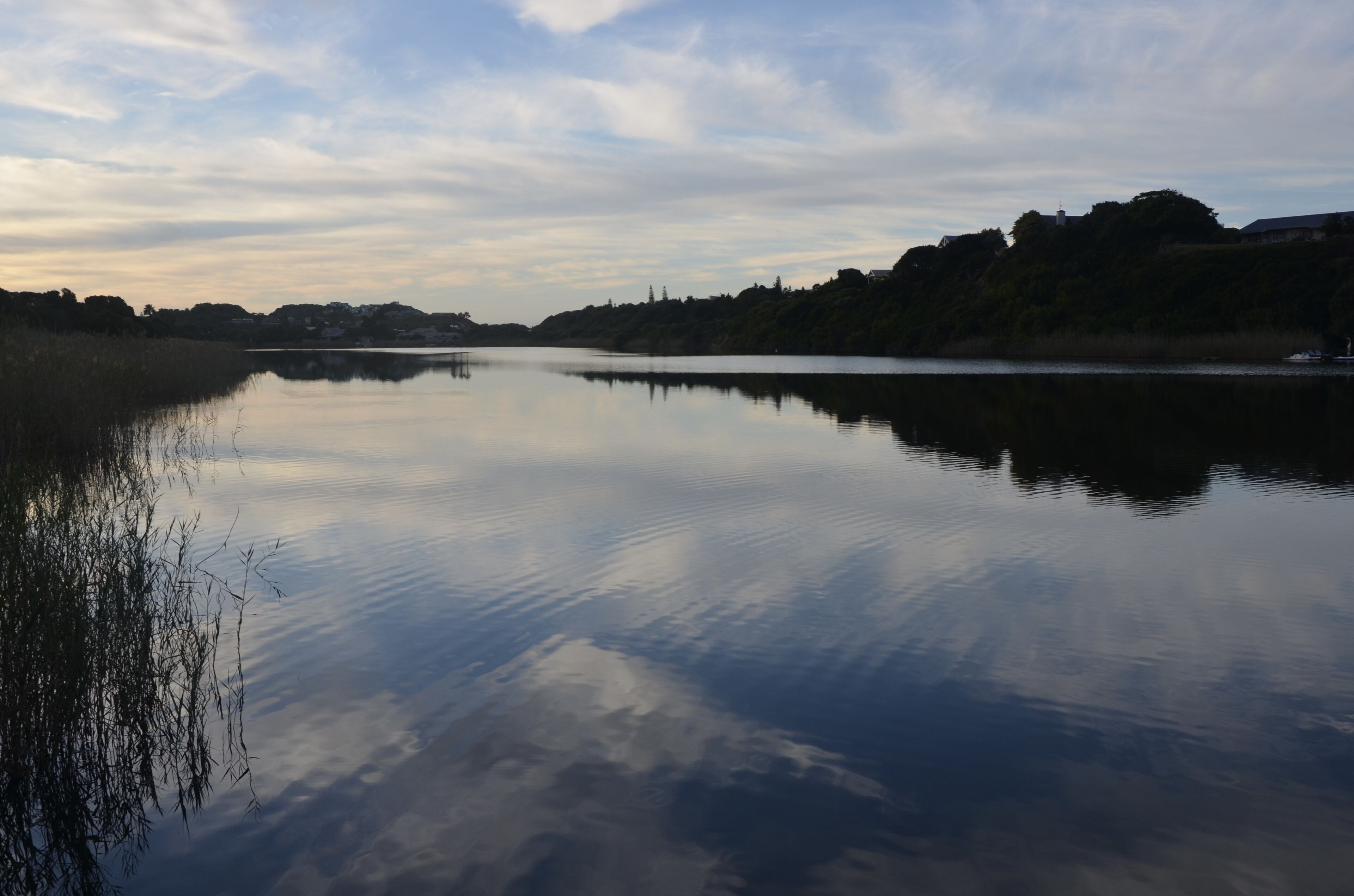 A calm lake with a clear reflection of the sky and surrounding landscape.