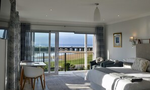 Habitación de hotel con una cama grande, un escritorio y una silla. Se ve la playa y el océano a través de las puertas de cristal.