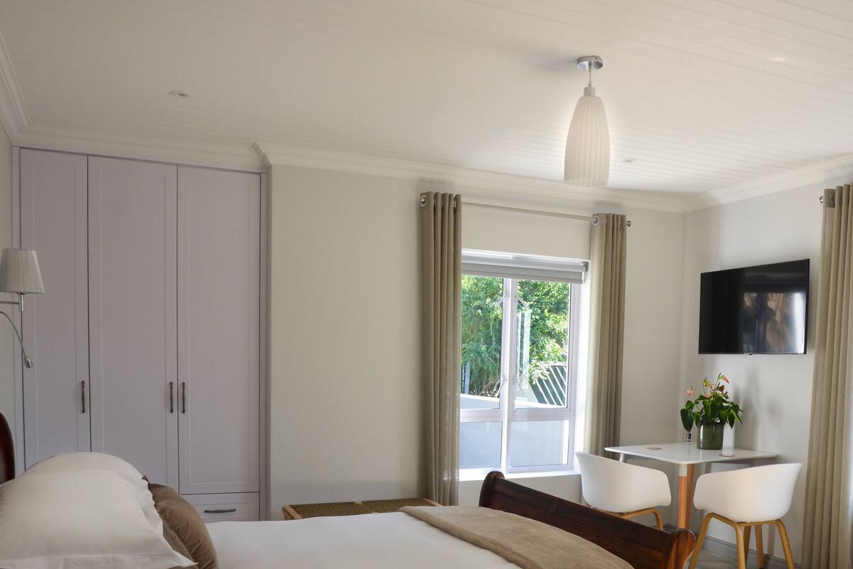 A hotel room with a bed, a desk, a chair, a TV, and a window with curtains.