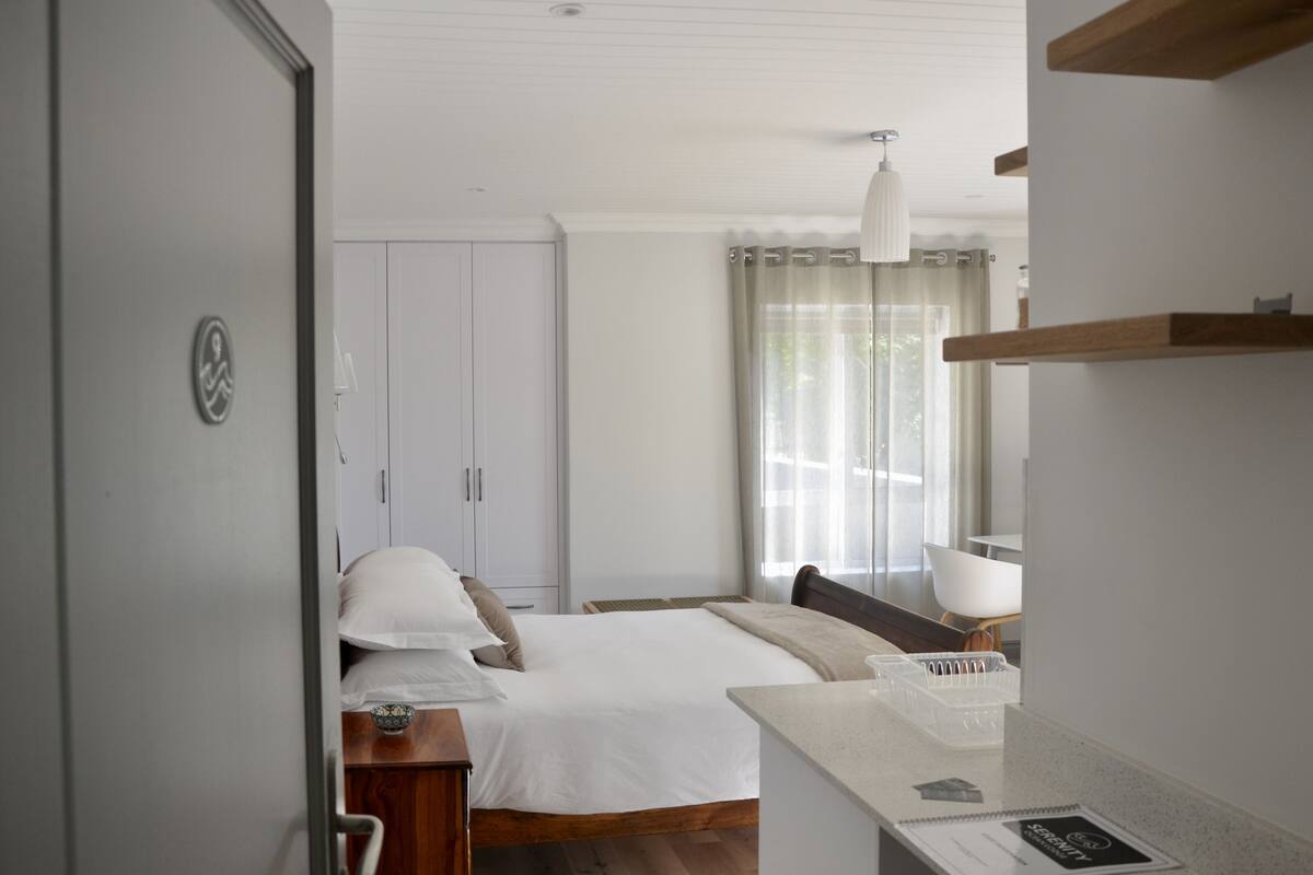 A hotel room with a bed, a bedside table, a lamp, and a window with curtains.