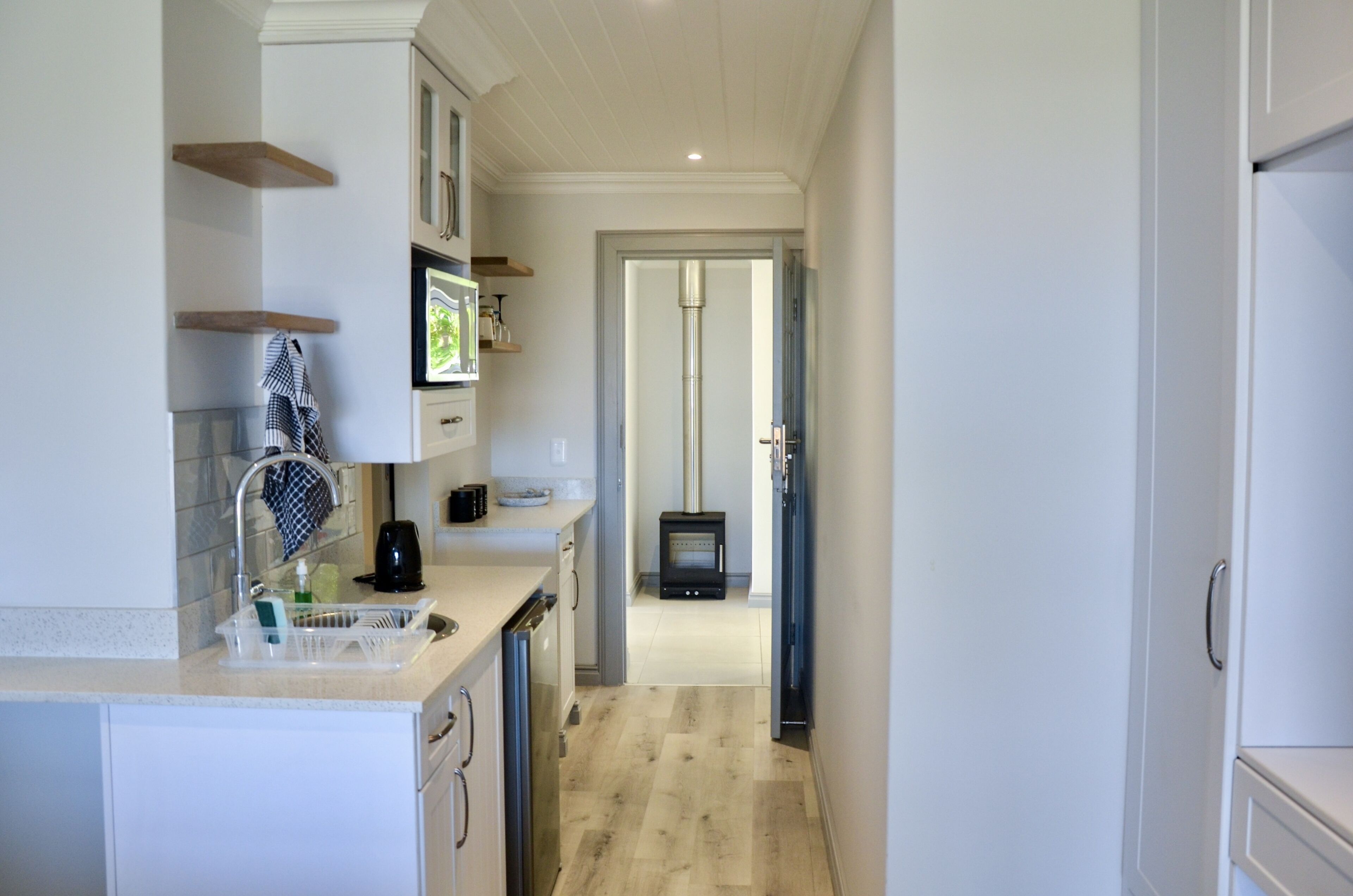 A narrow kitchen with white cabinets, a stainless steel sink, and a black stove in the background.