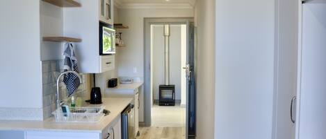 A narrow kitchen with white cabinets, a stainless steel sink, and a black stove in the background.