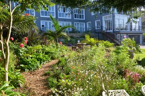 Un edificio moderno con un jardín delantero, que incluye un sendero, plantas variadas y un espacio para sentarse.