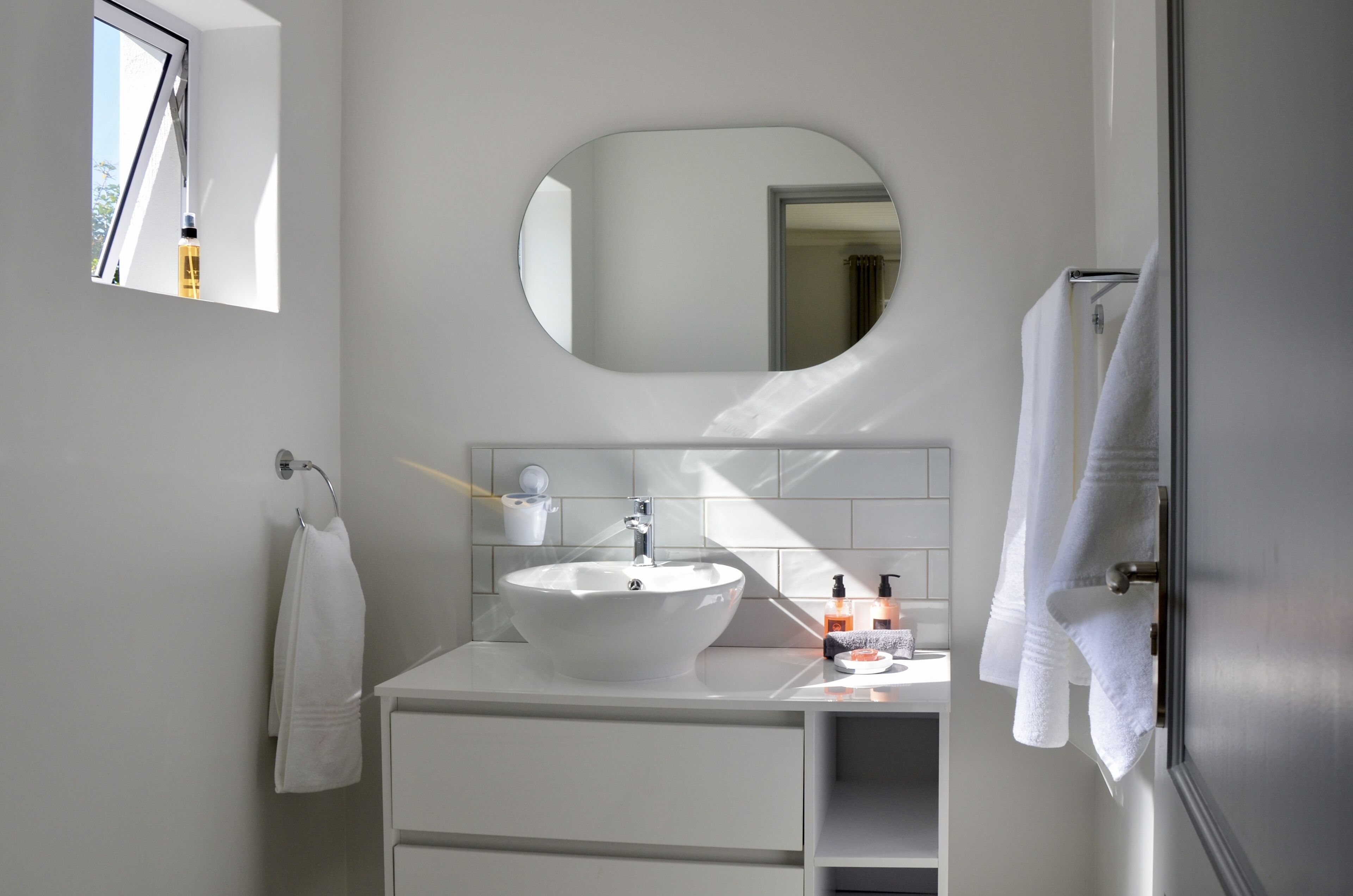 A modern bathroom with a white sink, a large mirror, and a towel rack.