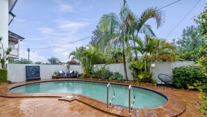 A swimming pool with a brick deck, surrounded by palm trees and plants.