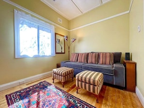 A living room with a sofa, two striped ottomans, a patterned rug, a window with curtains, and a mirror on the wall.
