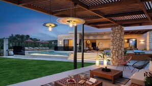 An outdoor patio with a pool, lounge chairs, and a stone pillar. - Mirena Luxury Living - Casa Di Ria (Αφάντου)