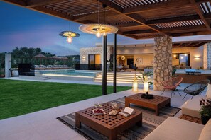 An outdoor patio with a pool, lounge chairs, and a stone pillar.