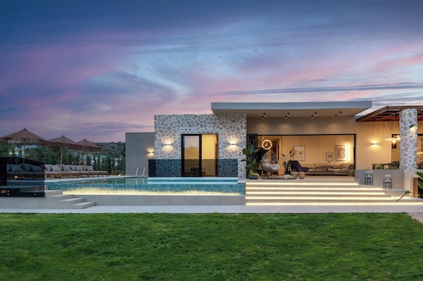 A modern house with a swimming pool, outdoor seating, and a well-lit interior.