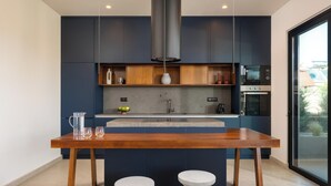 A modern kitchen with dark cabinets, a wooden table, and two stools. - Mirena Luxury Living - Casa Di Ria (Αφάντου)