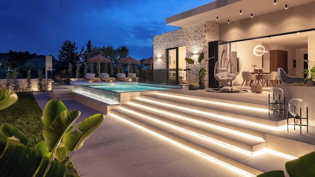 A modern outdoor pool area with steps leading to a seating area, surrounded by greenery. - Mirena Luxury Living - Casa Di Ria (Αφάντου)