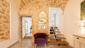 Un couloir aux murs de pierre, avec une chaise violette et un escalier.