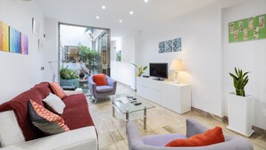 A modern living room with a glass coffee table, a sofa, a chair, and a TV on a white cabinet. - Ca Se Predine by Rentallorca (Alcúdia)