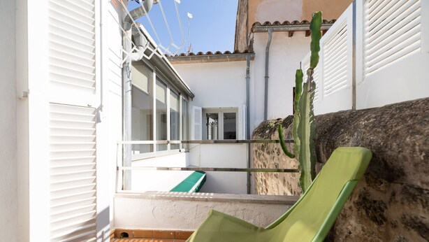 Un petit espace extérieur avec une chaise verte, un cactus et un sol carrelé.