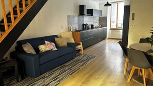 Un salon moderne avec un canapé bleu foncé, un escalier en bois, un coin cuisine doté de meubles gris et une table à manger avec des chaises.