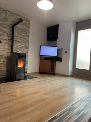 A modern living room with a wood-burning stove, a flat-screen TV, and a large window. - "La Maison d'Hugo" Comfortable & Spacious (Moirans-en-Montagne)
