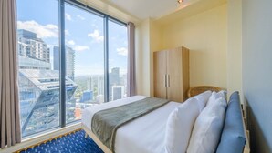 Quarto de hotel com uma grande janela, uma cama, um guarda-roupa e vista para a cidade.