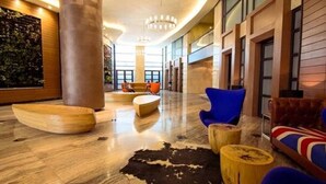 Um lobby com uma grande escultura de madeira, uma poltrona azul, um sofá de couro e um tapete de couro de vaca.