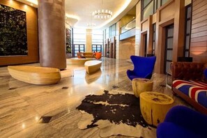 Un vestíbulo con una gran escultura de madera, un sillón azul, un sofá de cuero y una alfombra de piel de vaca.