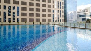 Piscina com borda azulejada, cercada por um edifício com grade de janelas e fachada de vidro.