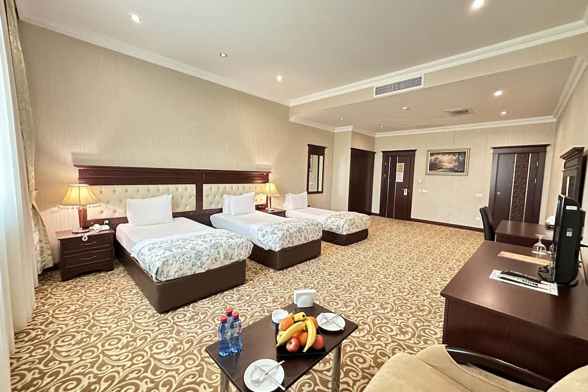 A hotel room with two beds, a desk with a fruit tray, and a TV.