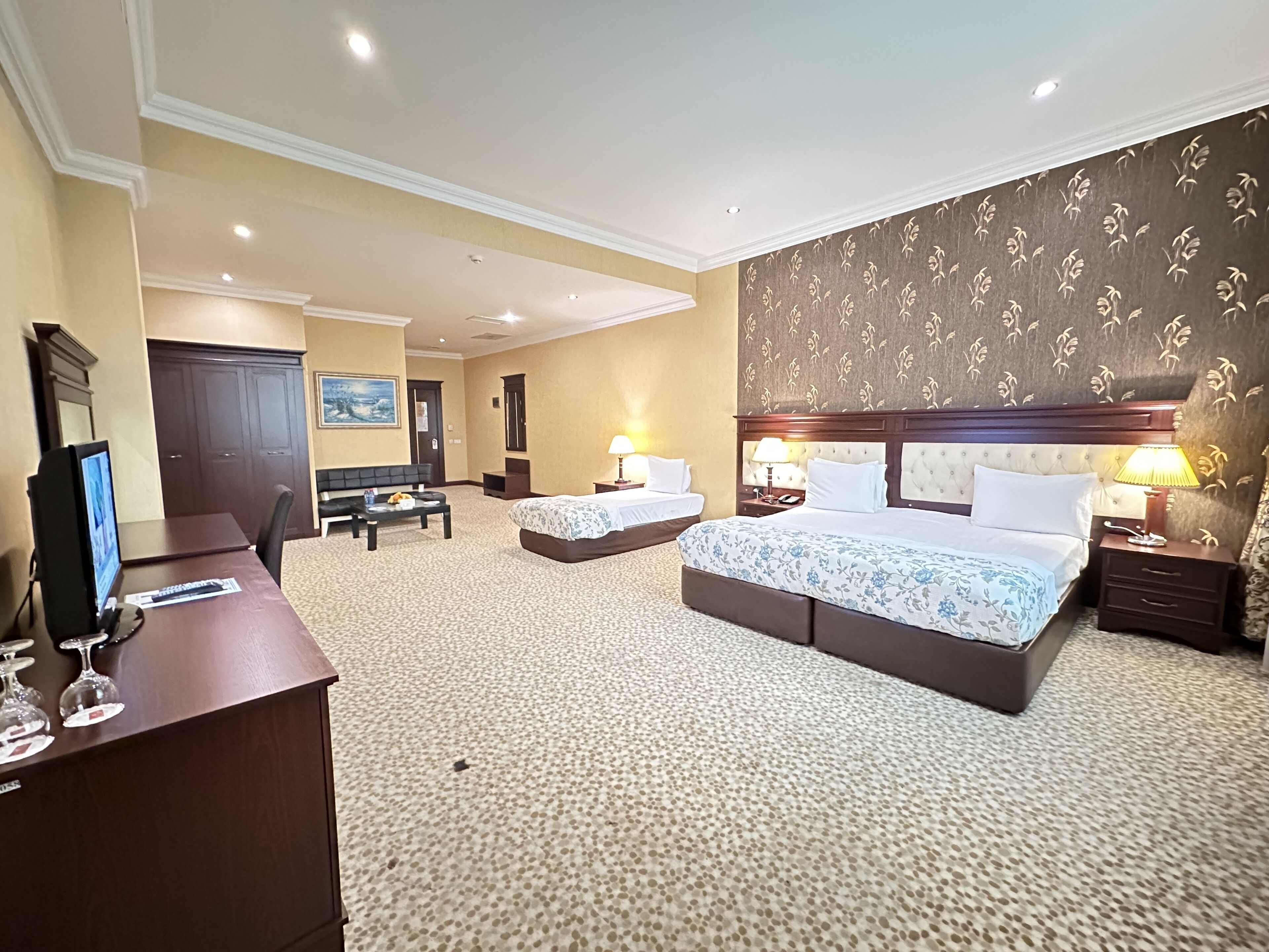 A hotel room with two beds, a desk with a computer, a TV, and a dining table with chairs.