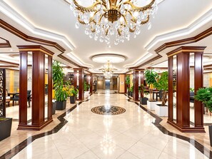 A hotel lobby with a grand chandelier, wooden columns, and potted plants. - Modern Hotel - Baku (Baku)